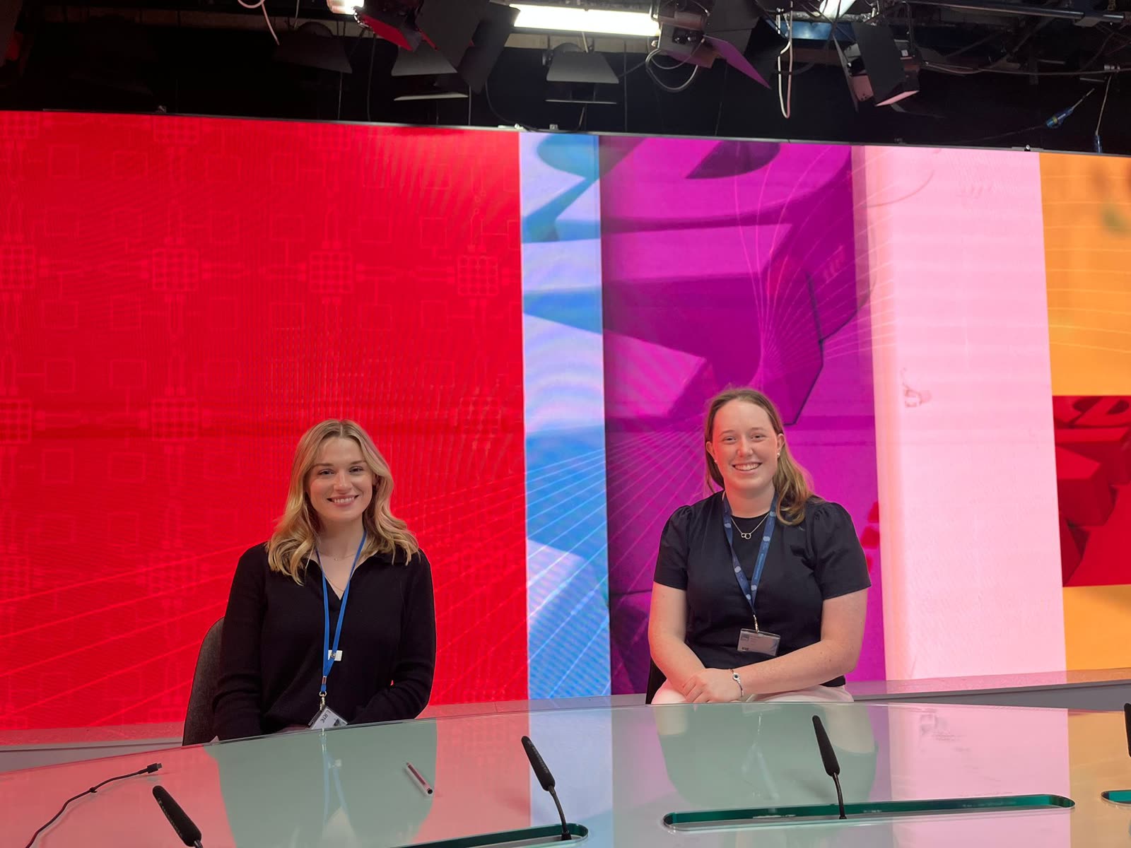Orla at a television studio desk, lanyard on, ready to go live